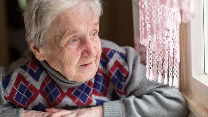 An elderly woman looking through a window.