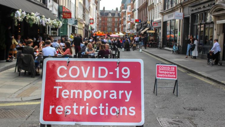 Photograph of a red sign in the middle of a street that reads "COVID-19 Temporary Restrictions".